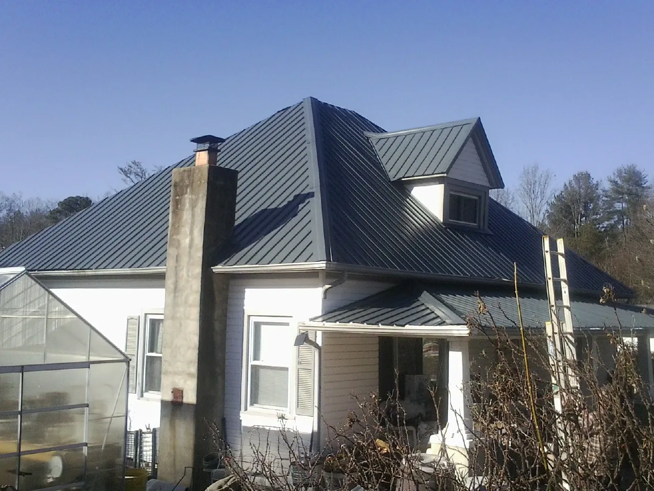 Dark blue standing seam metal roof on a white farmhouse with dormer — Slate & Tile Roof Repair by Roofing Brothers in Lake Alfred