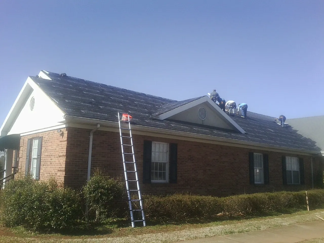 Crew tearing shingles off a brick ranch roof with a ladder set — Emergency Roof Repair work by our crew in Lake Alfred