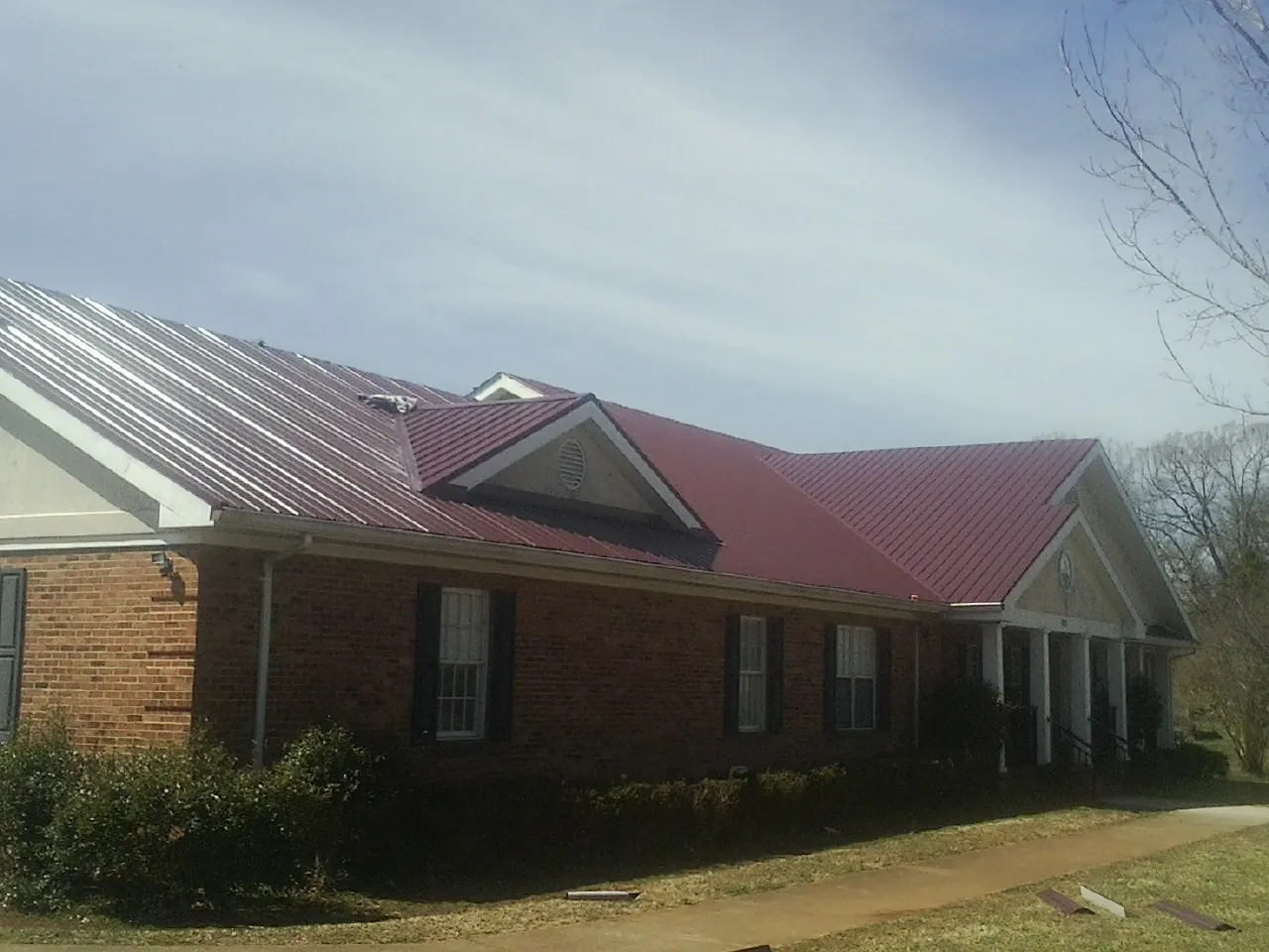 Red metal roof with gabled entries on a long brick building, from a Hail Damage Roof Repair job in Lake Alfred