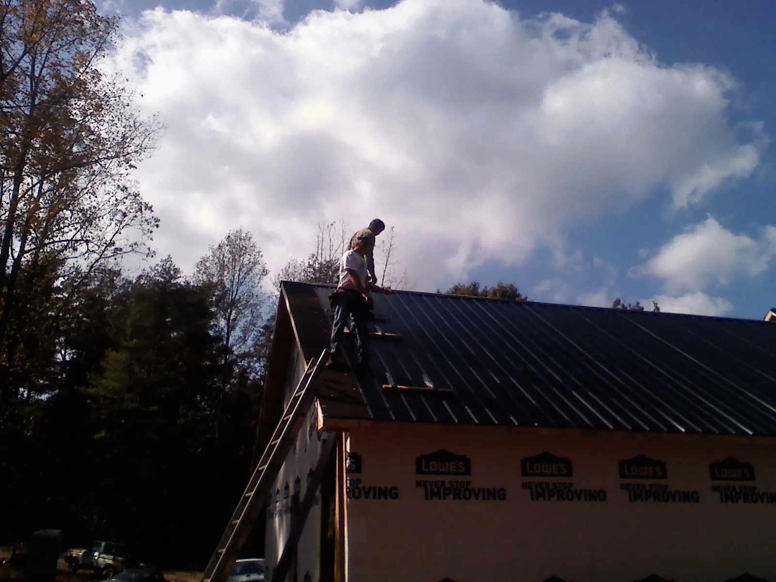 Roofer fastening dark metal panels high against a cloudy sky, from a Roof Inspection job in Lake Alfred