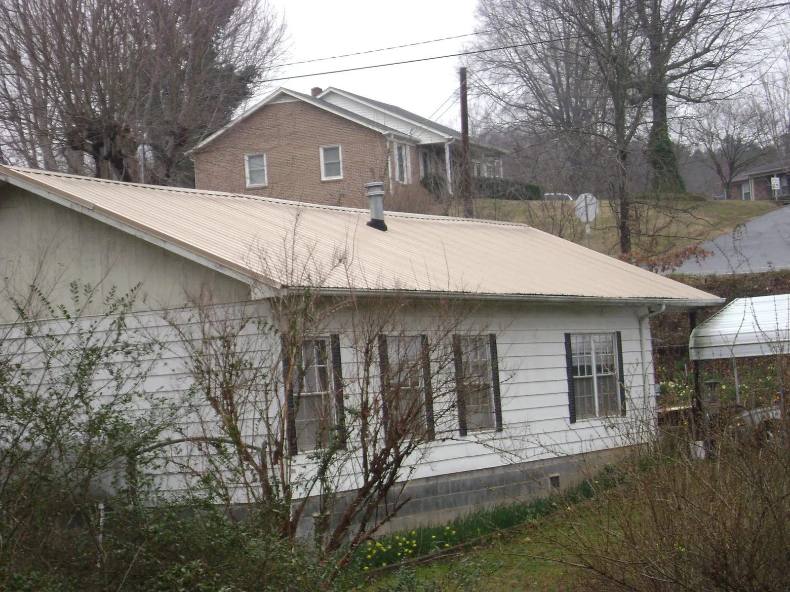 Tan metal roof on a white sided house set into a hillside — Commercial Roofing by Roofing Brothers in Lake Alfred